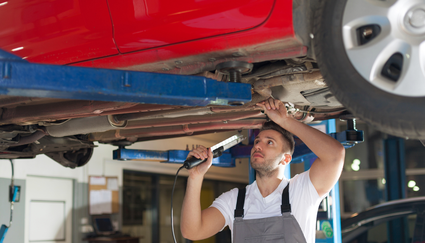 Ung mannlig mekaniker som jobber under oppheist bilunderstell